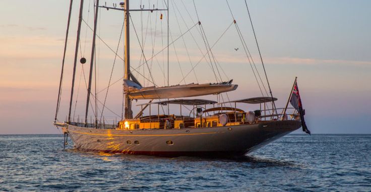 a sailboat sailing in the ocean at sunset with people on it's deck