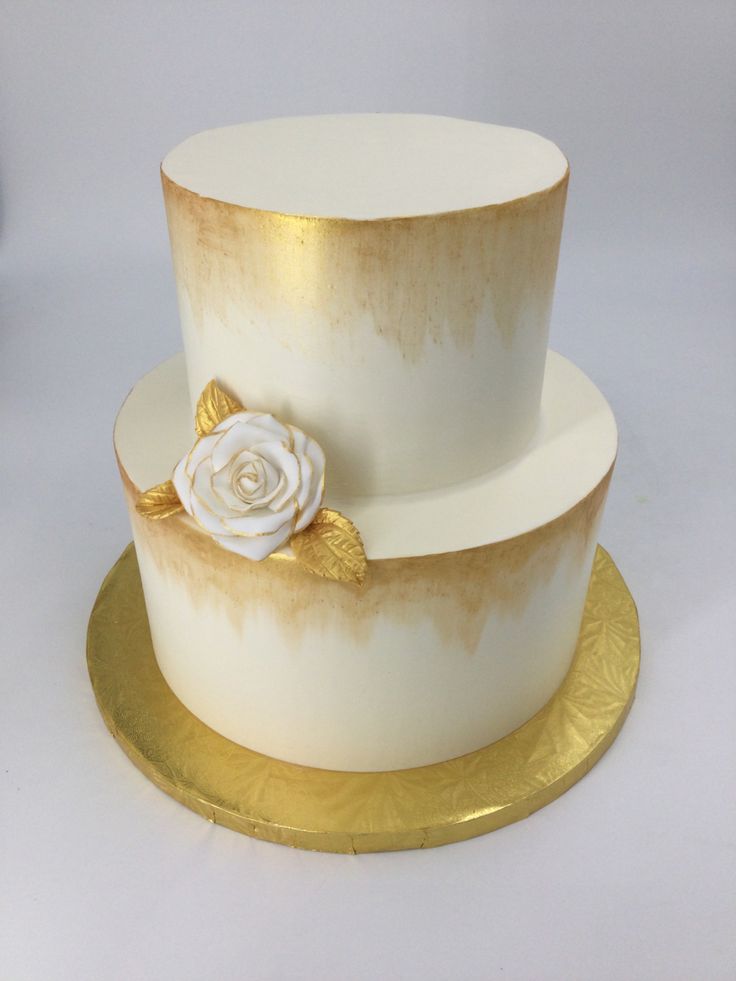 a white and gold wedding cake with a rose on the top, sitting on a golden platter