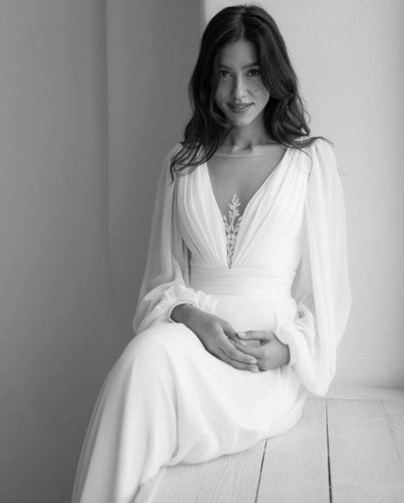 a woman in a long white dress sitting on a wooden floor posing for a photo