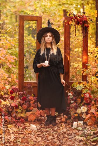 a woman wearing a witches hat and black dress standing in front of a wooden gate