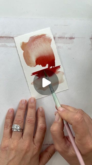 two hands holding a paintbrush and painting a piece of paper with red ink on it