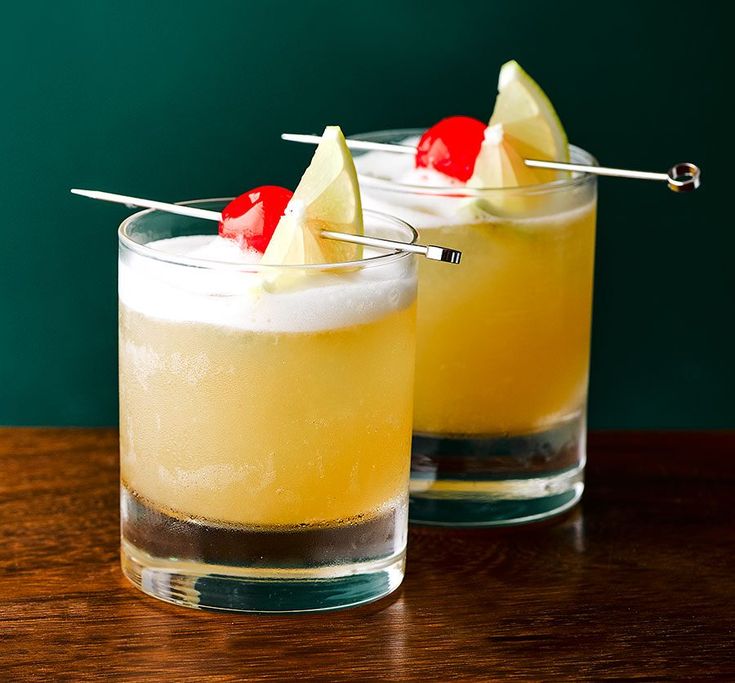 two glasses filled with drinks sitting on top of a wooden table