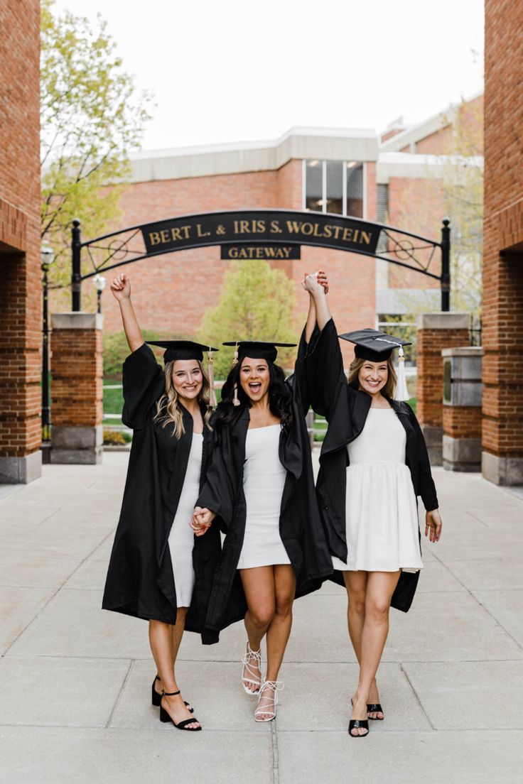 three women in graduation gowns and caps holding up their arms while posing for the camera