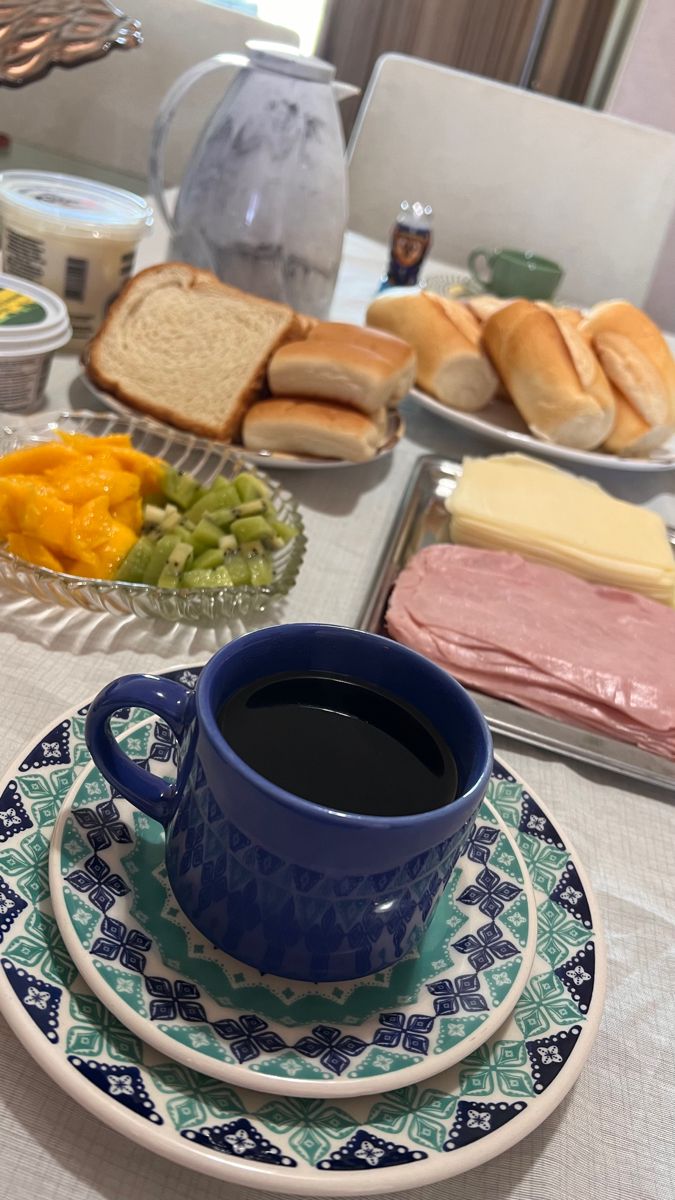 a cup of coffee sitting on top of a blue and white plate next to sandwiches