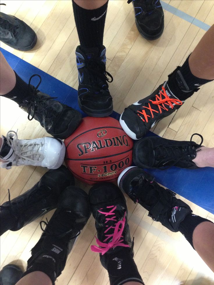 a group of people standing around a basketball on top of a hard wood floor with their feet in the air