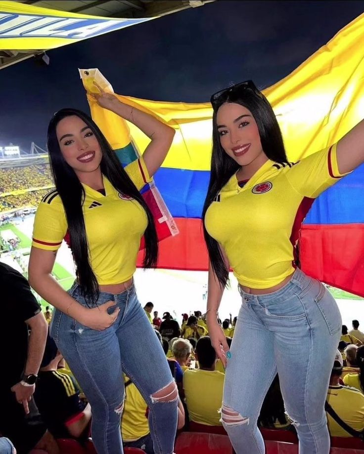 two beautiful women standing next to each other in front of a large flag at a soccer game