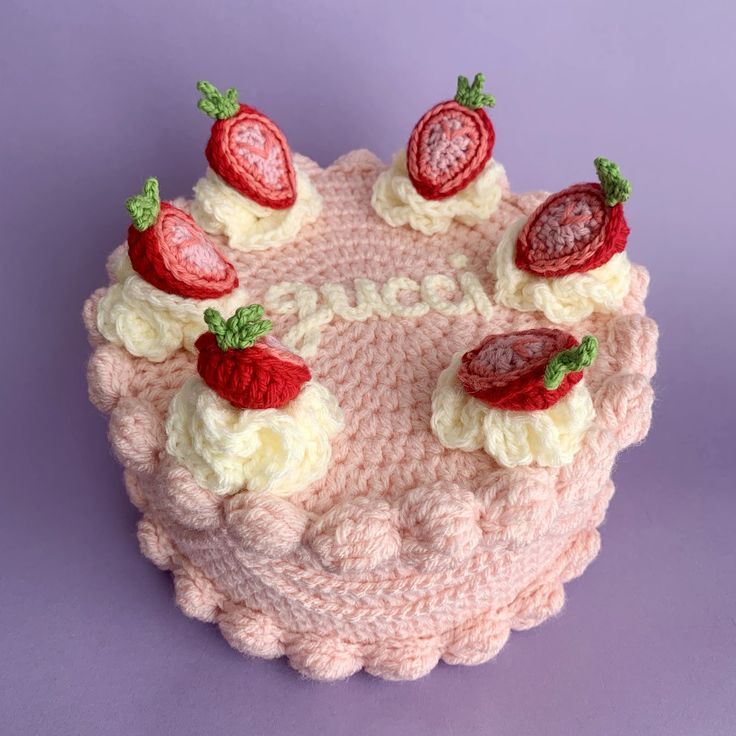 a crocheted cake with strawberries and cream frosting is on a purple surface