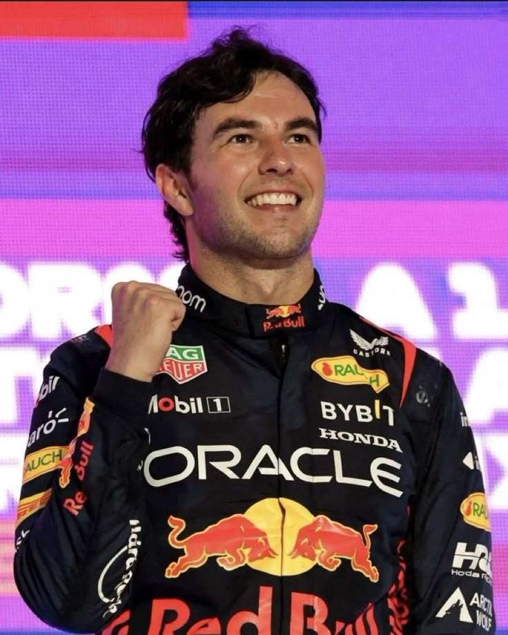 a man standing on top of a stage with his fist in the air and wearing a red bull uniform