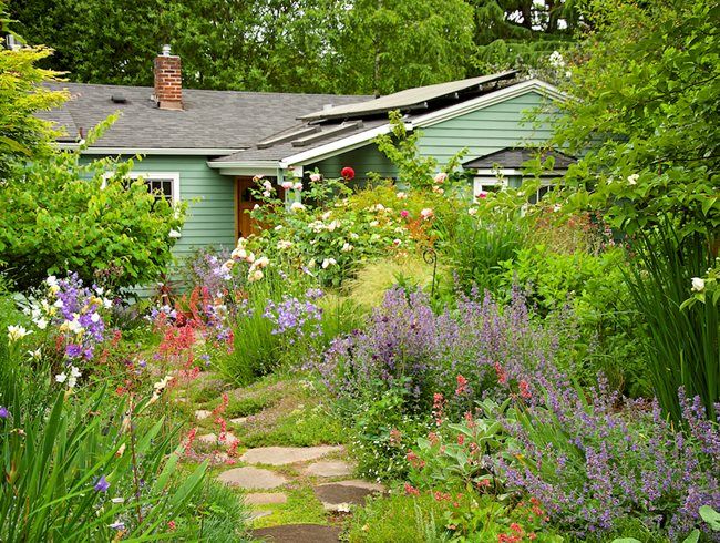 a green house surrounded by lots of flowers and greenery on the side of it