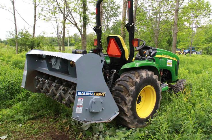 a green tractor parked in the grass near trees