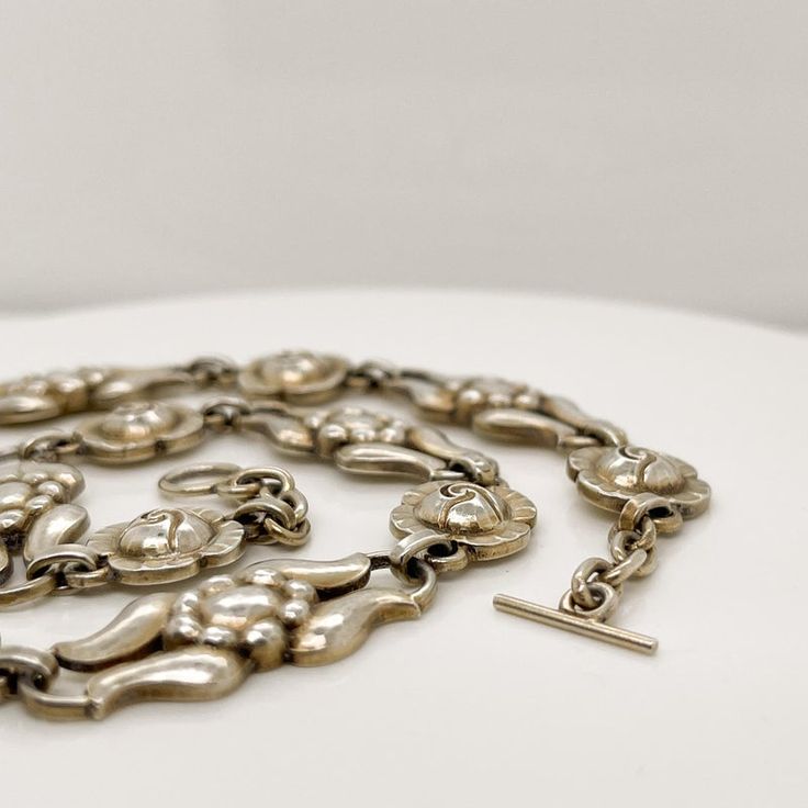 A very fine Georg Jensen necklace in sterling silver.  Model No. 10.  With alternating rose and stylized floral links, traces of its original gilding, and a toggle clasp.  Designed by Georg Jensen and bearing an old GI mark.  At approximately 14 1/2 in., the necklace is a snugly fitting, true choker.  Simply a great piece!  Date: 20th Century  Overall Condition: It is in overall good, as-pictured, used estate condition.  Condition Details: The links appear to retain some of an original gilding o Vintage White Gold Metal Necklace, Antique Jewelry With Polished Oval Link Finish, Antique Oval Link Jewelry With Polished Finish, Vintage Metal Necklace With Polished Finish, Victorian Hallmarked Link Necklace, Victorian Link Necklace Hallmarked, Silver Link Necklace With 17 Jewels, Antique Silver Necklace With Polished Finish, Vintage White Gold Necklace With Sterling Silver Clasp