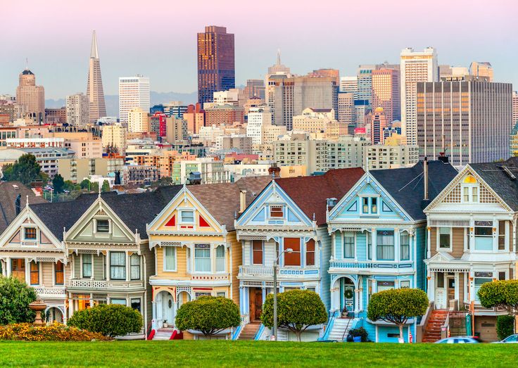 a row of painted victorian homes in san francisco, california with the city skyline in the background