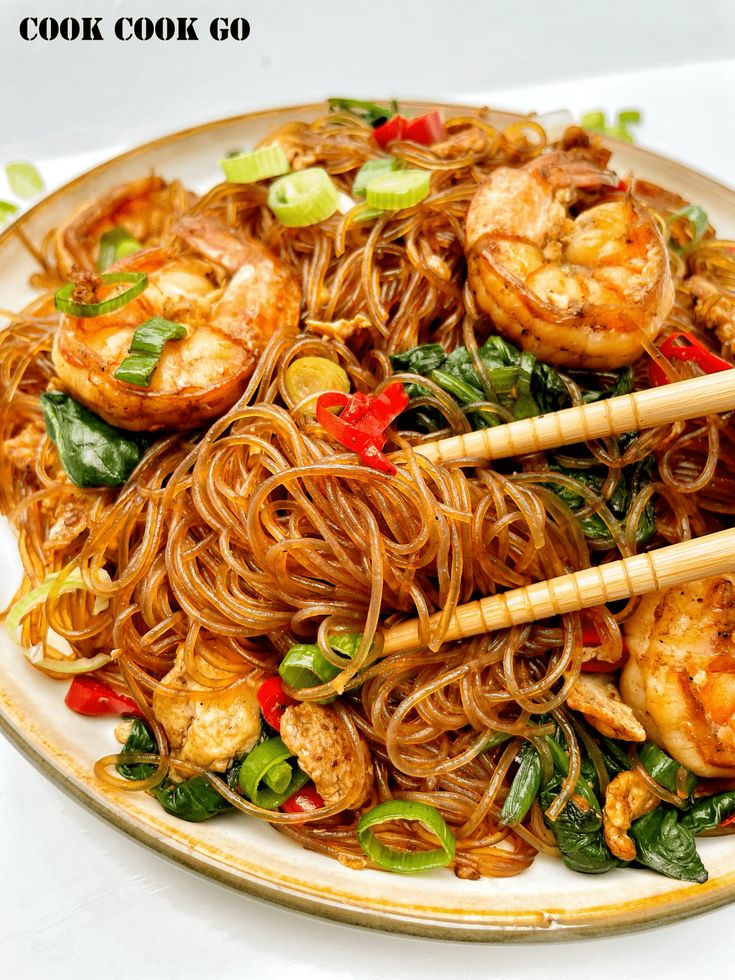 a plate full of noodles with shrimp and spinach on it, topped with chopsticks