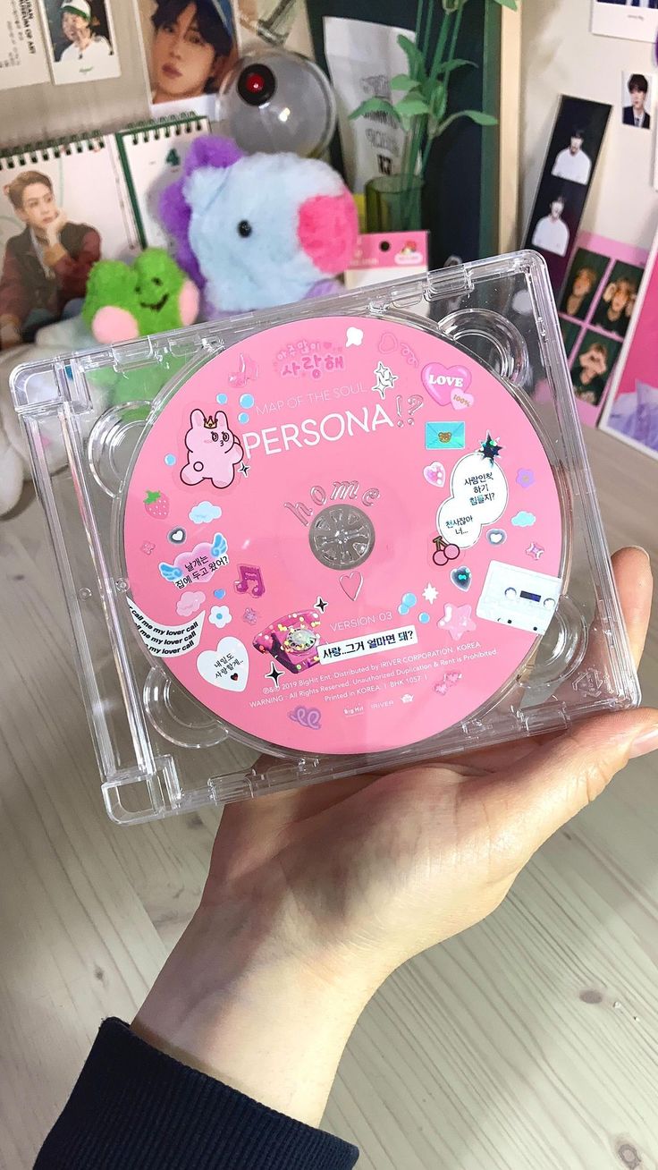 a person holding up a pink cd case with stickers on it's side