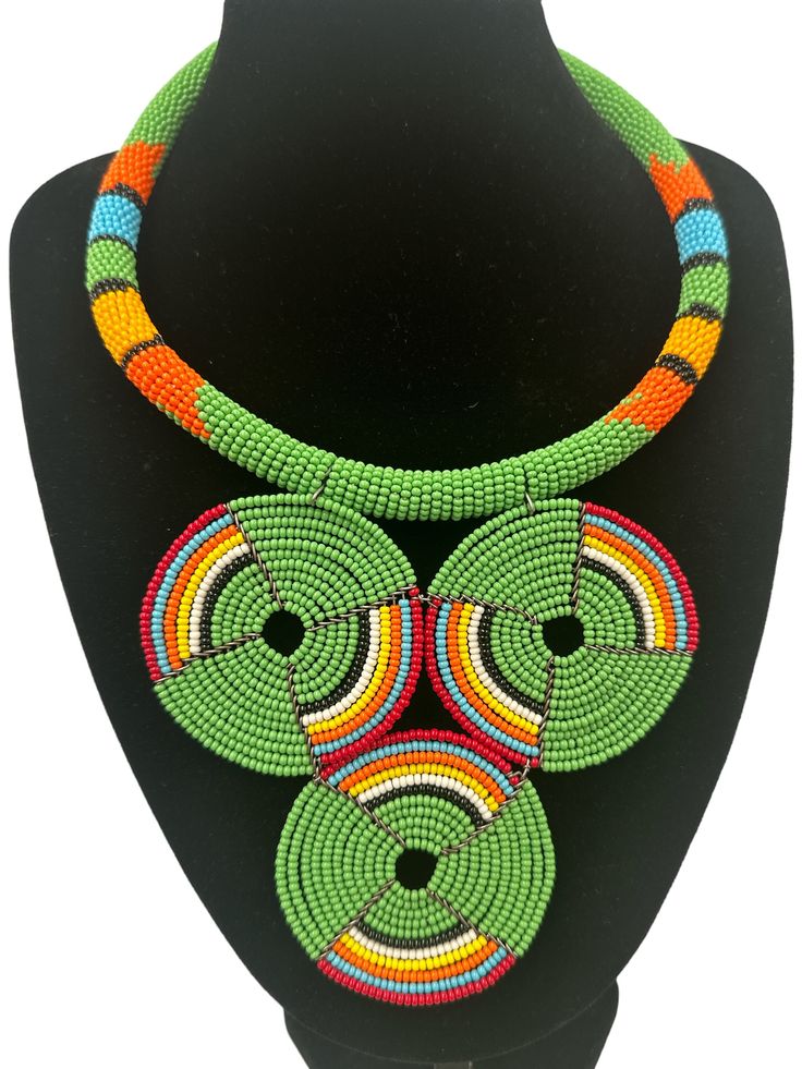 This stunning African necklace showcases a beautiful green beaded disc pendant that is truly authentic. The pendant is handcrafted and features intricate beading detail that is sure to impress. The necklace is perfect for those who appreciate the fine craftsmanship and unique jewellery. The beaded pendant is eye-catching and adds a touch of elegance to any outfit.  The diameter of the pendant - 5 inches. Neck Width - 16 inches. Adjustable Green Artisan Jewelry, Green Adjustable Artisan Jewelry, Artisan Adjustable Green Jewelry, Traditional Green Adjustable Necklace, Bohemian Green Pendant Beaded Necklace, Green Beaded Necklace With Round Pendant, Bohemian Green Beaded Pendant Necklace, Green Adjustable Round Pendant Jewelry, Traditional Green Round Jewelry