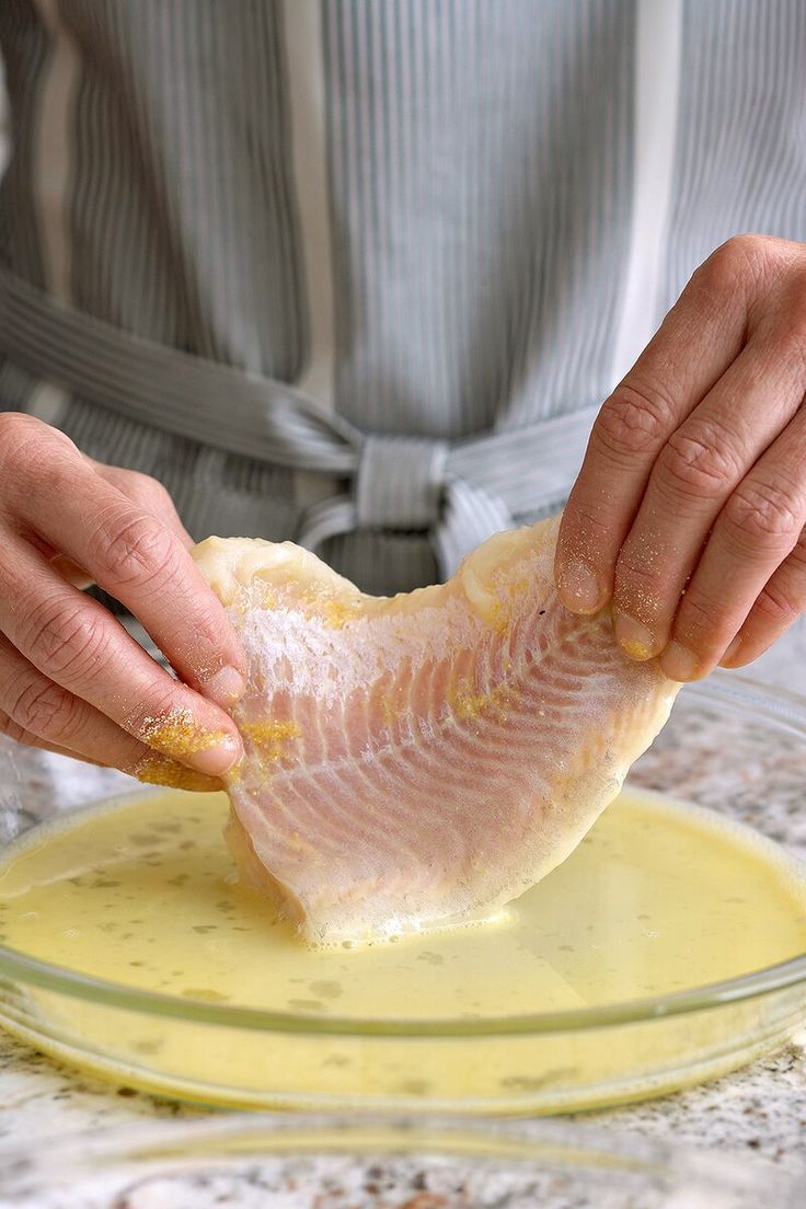 a person in an apron is preparing fish on a plate with sauces and butter