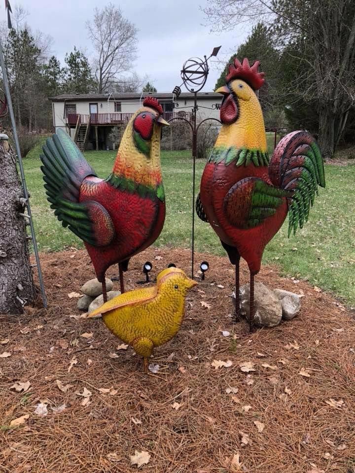 two colorful rooster statues standing next to each other on top of a pile of dirt