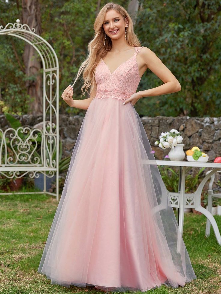 a woman wearing a pink dress standing in front of a table with flowers on it