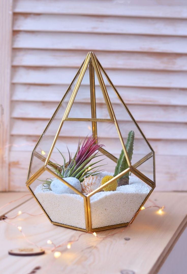 a gold geometric terrarium with succulents and lights in it on a table