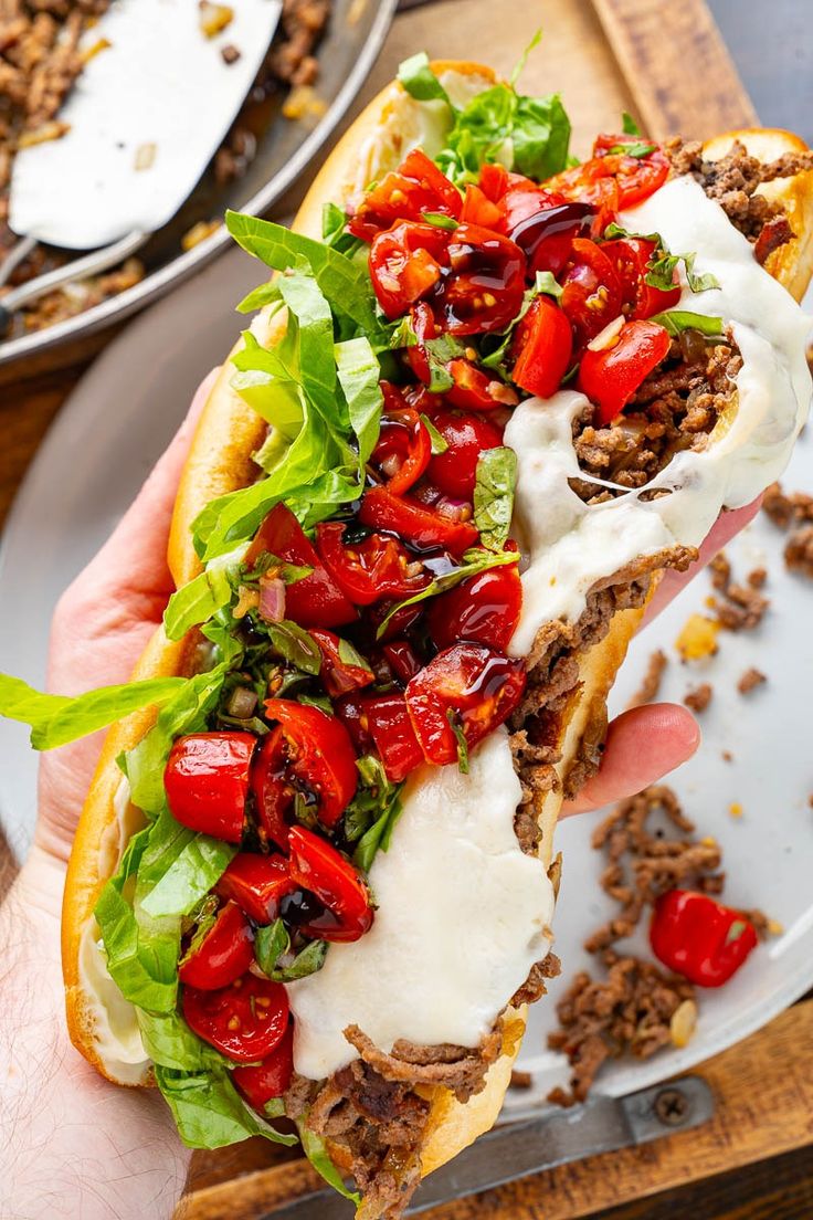 a hand holding a sandwich with meat, tomatoes and lettuce on it in front of other plates