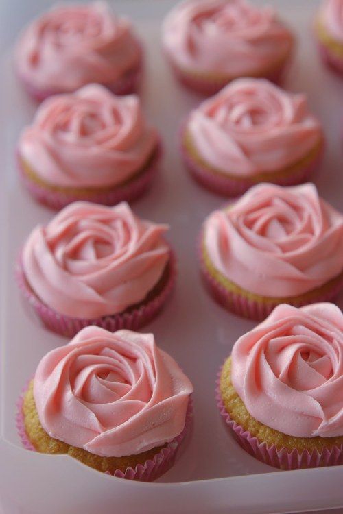 cupcakes with pink frosting sitting in a white tray on top of a table