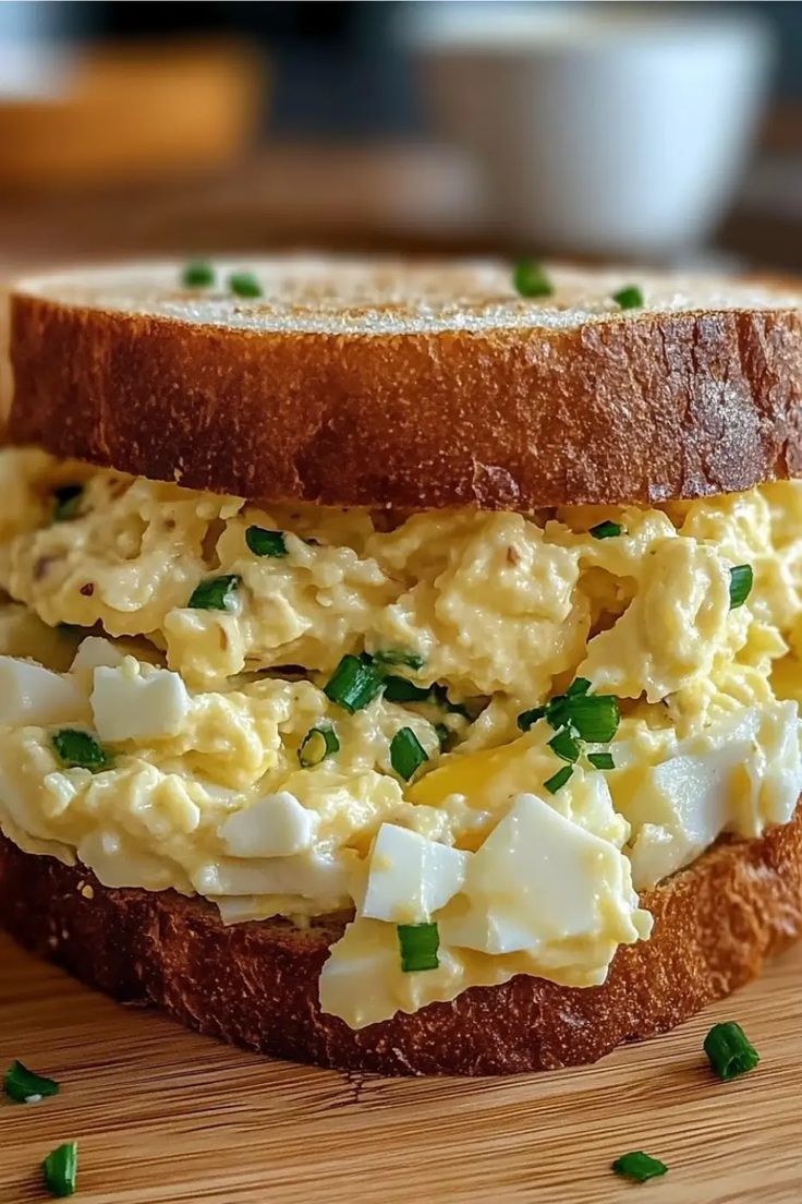 an egg salad sandwich on a wooden cutting board