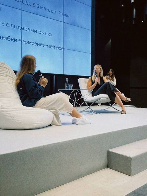 two women are sitting on the stage with their phones in their hands and one is taking a photo