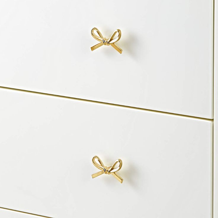 two white drawers with gold handles and bows on the top one drawer is closed to reveal a pair of scissors