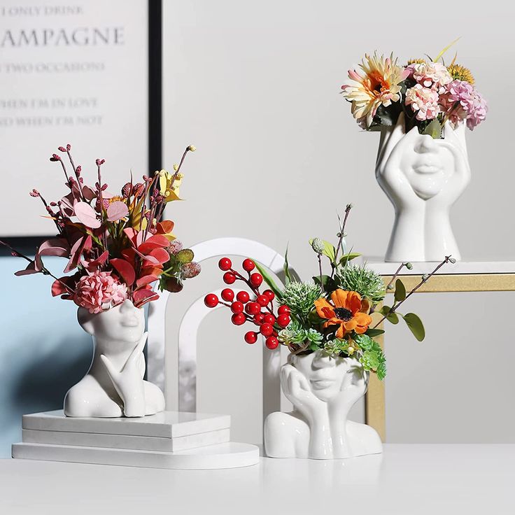 two white vases with flowers in them sitting on a table next to each other