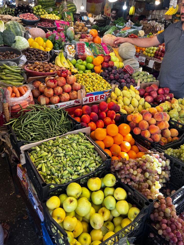 a man standing in front of a large display of fruits and vegetables at a market