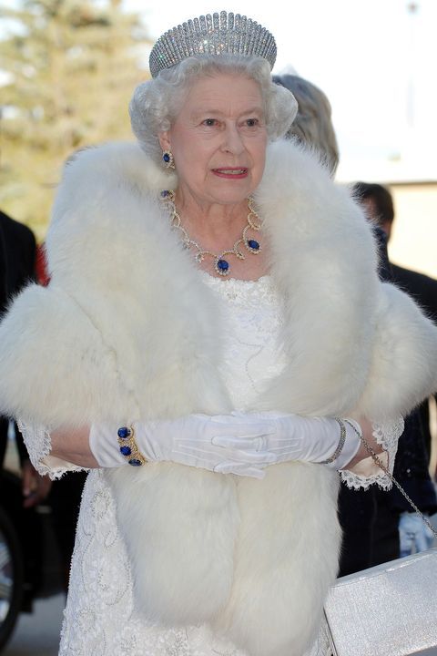 an older woman in a white dress and fur stoler walking down a pink carpet