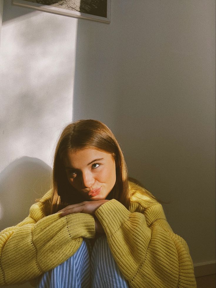 a woman in a yellow sweater leaning against a wall