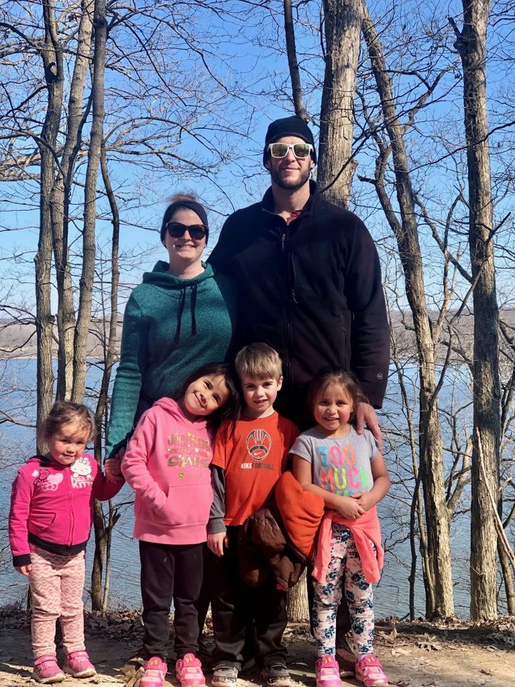 a man and two children standing next to each other in front of trees with the water behind them