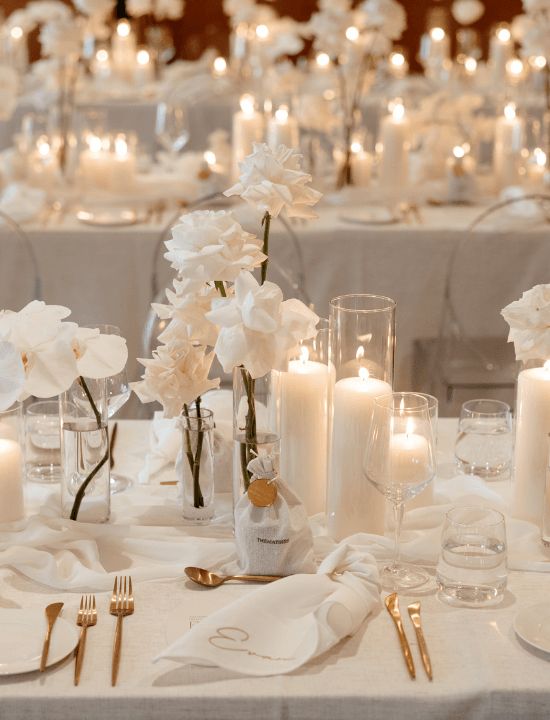 the table is set with white flowers, candles and silverware for an elegant wedding reception