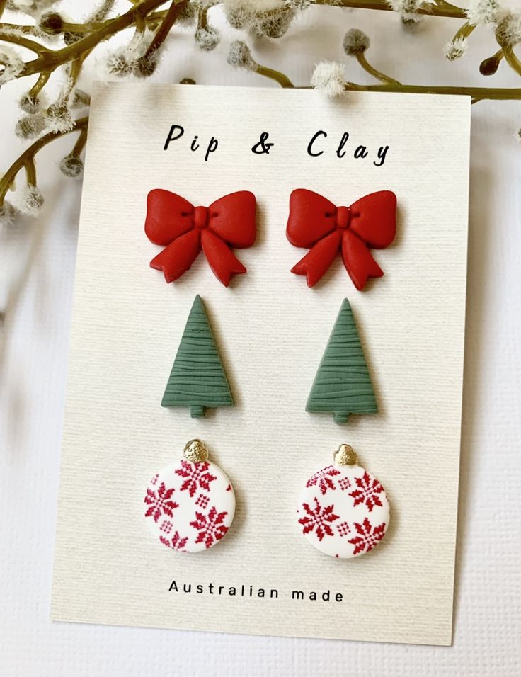 two christmas tree shaped earrings with bows on the top and bottom, sitting in front of a card