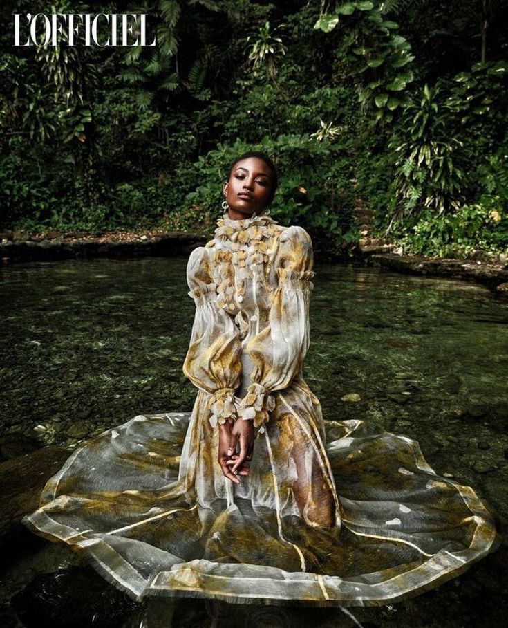 a woman sitting on top of a body of water in front of trees and bushes