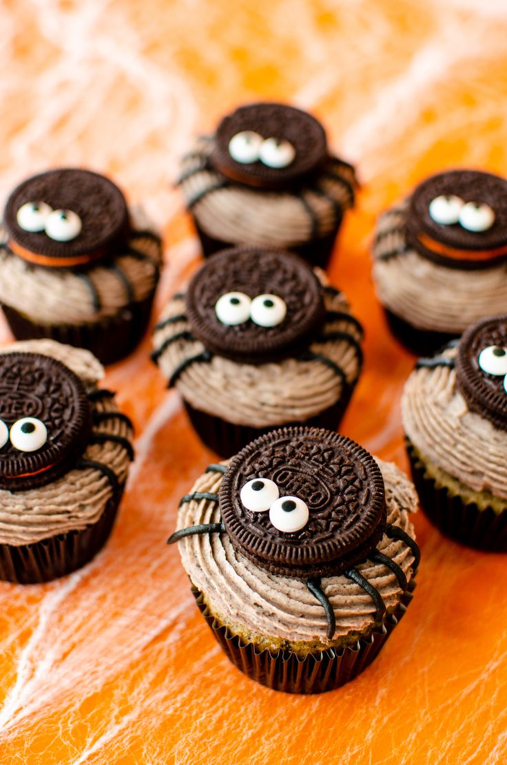 chocolate cupcakes decorated with oreo cookies and spider eyes on an orange surface