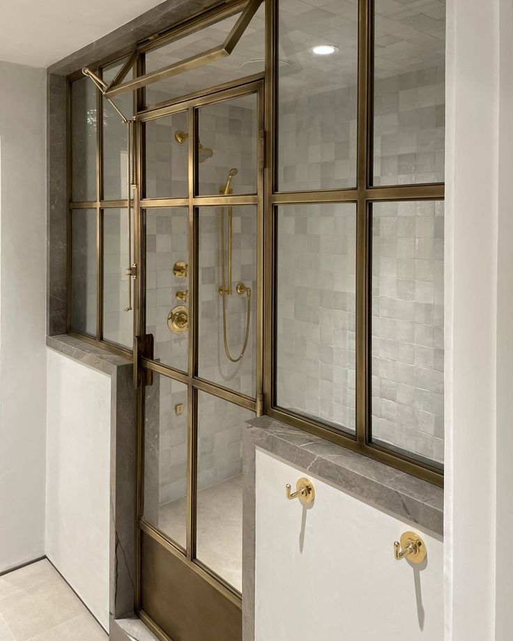 an open shower door in a bathroom with white tile and gold fixtures on the wall