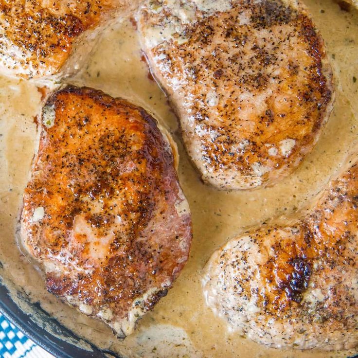 four pieces of meat sitting on top of a pan covered in brown gravy