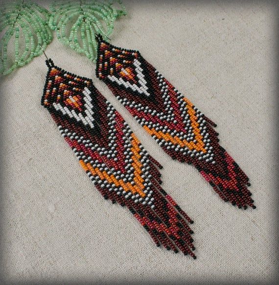 two red and yellow beaded earrings with green leaves on the bottom one is made from seed beads