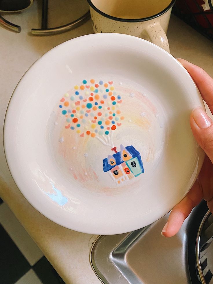 a person holding a white plate with colorful dots on it and a house painted on the side