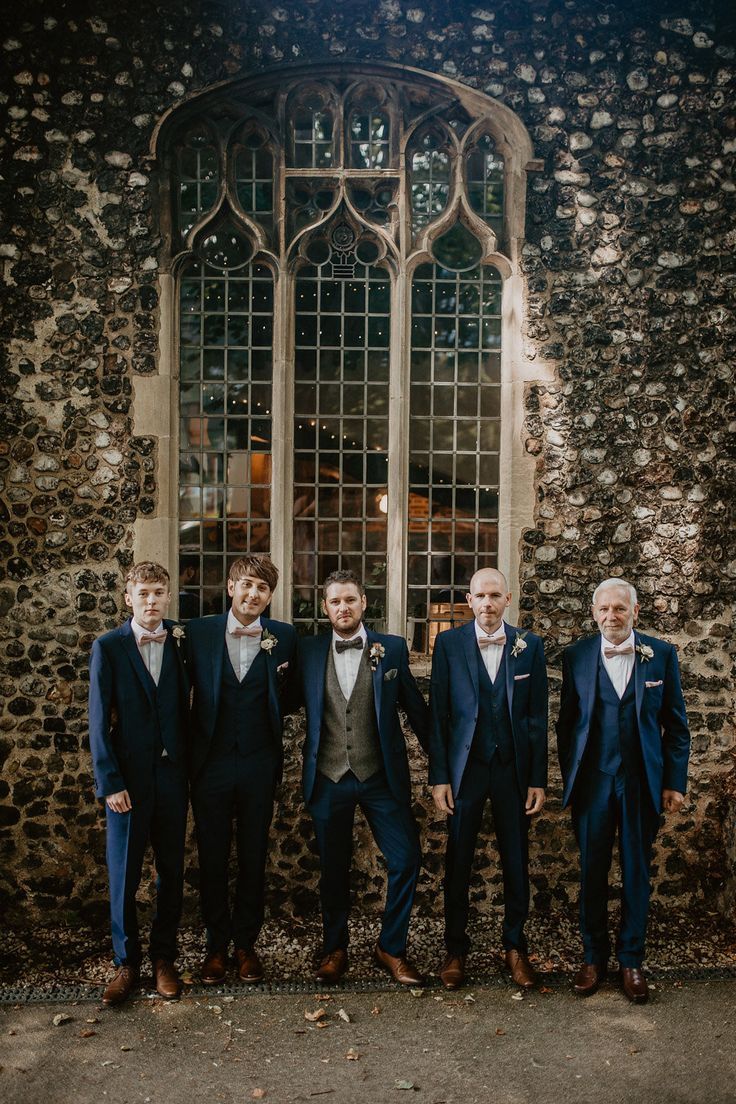 a group of men standing next to each other in front of a stone wall and window