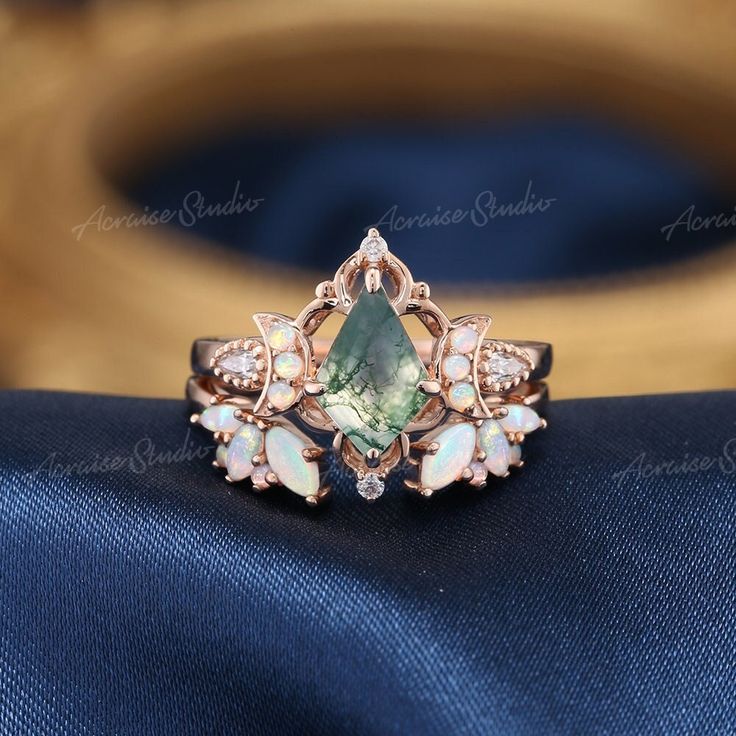 an engagement ring with green and white stones on it's side, sitting on top of a blue cloth