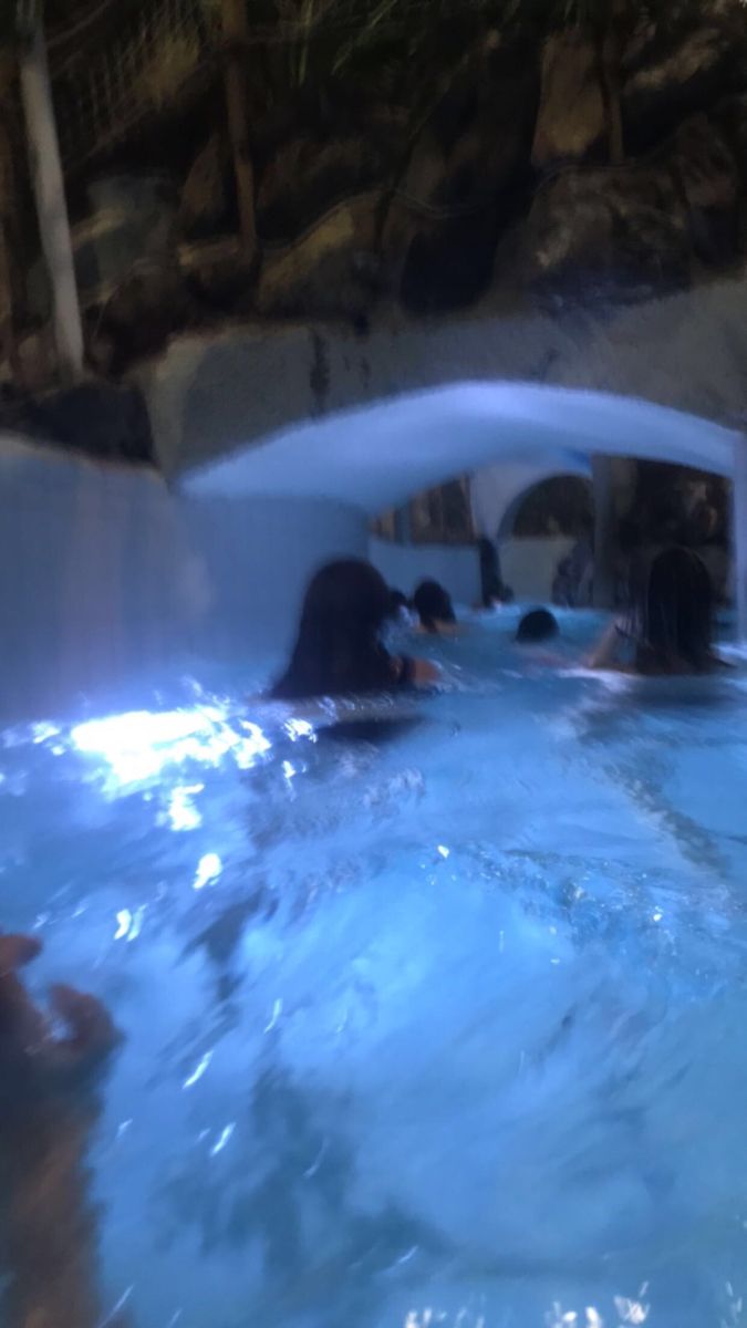 some people are swimming in the water inside an indoor pool with rocks and plants on the sides