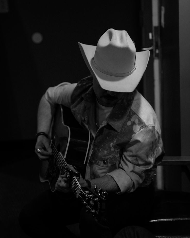 a man with a cowboy hat playing an acoustic guitar