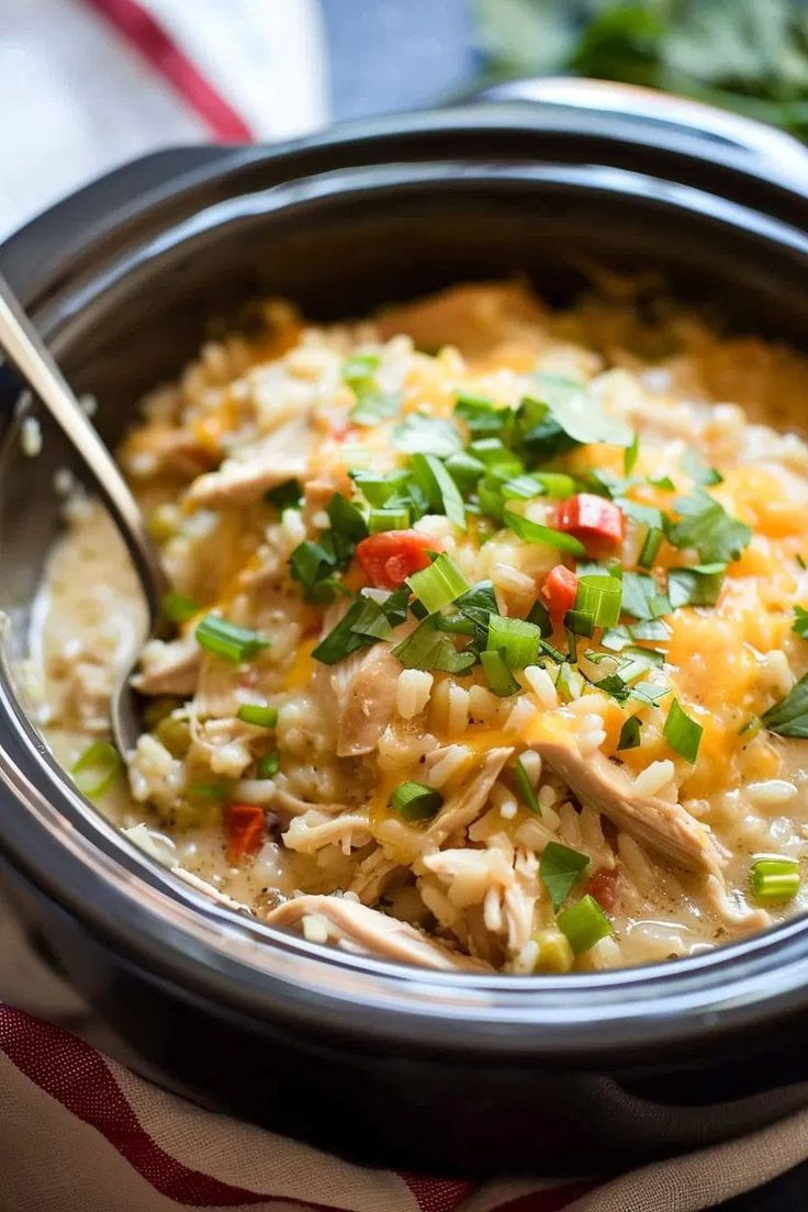 a crock pot filled with chicken and rice topped with green onions, cilantro