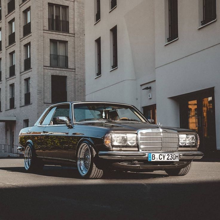 an old black car parked in front of a tall building on the side of the road