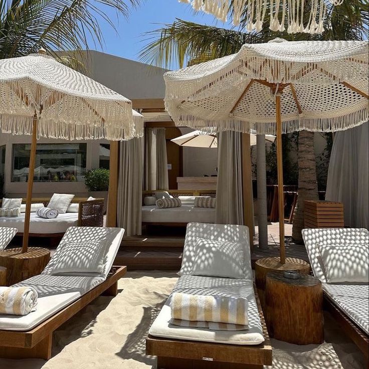 lounge chairs and umbrellas on the sand under palm trees in front of a hotel