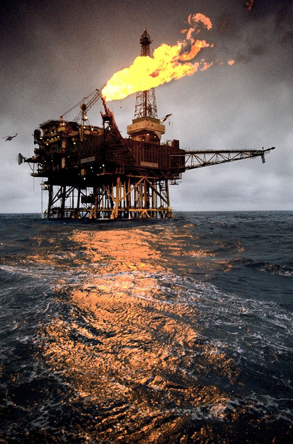 an oil rig on fire in the middle of the ocean with dark clouds above it