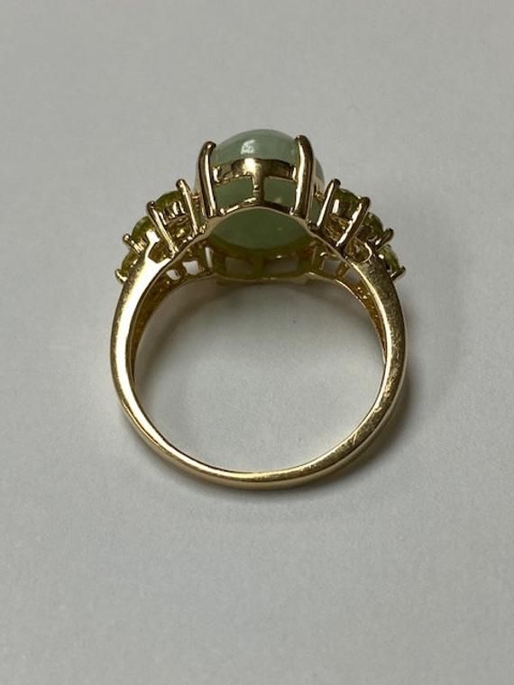 Lady's 14 karat yellow gold ring, with a large oval green jadeite jade at the center and accented by 12 round full cut natural peridot gemstones. The jade measures 14.0 mm x 10.0 mm with a depth of 4.65mm. The 12 round peridot measure approximately 2.5mm each. The ring is a size 8 and can be sized up or down. The ring weighs 4.72 grams. The ring is from an estate here in Hawai'i. The item is C11870/2 Please let me know if you have an questions. Mahalo for looking at my item. Oval Green Emerald Ring With Gemstone Accents, Oval Multi-stone Emerald Ring, Oval Green Multi-stone Gemstones, Green Oval Multi-stone Gemstones, Green Multi-stone Oval Cabochon Jewelry, Green Oval Cabochon Ring With Accent Stones, Green Oval Cabochon Ring With Center Stone, Green Oval Prehnite Rings, Round Green Prehnite Jewelry